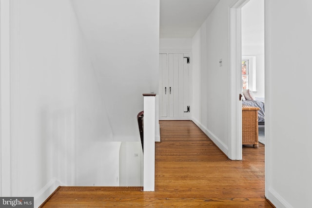 corridor featuring baseboards, wood finished floors, and an upstairs landing