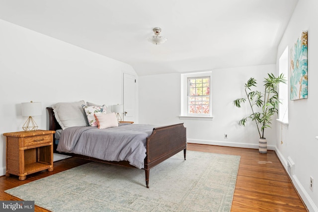 bedroom featuring baseboards, wood finished floors, visible vents, and vaulted ceiling