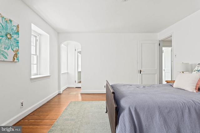 bedroom with light wood-style floors, arched walkways, and baseboards