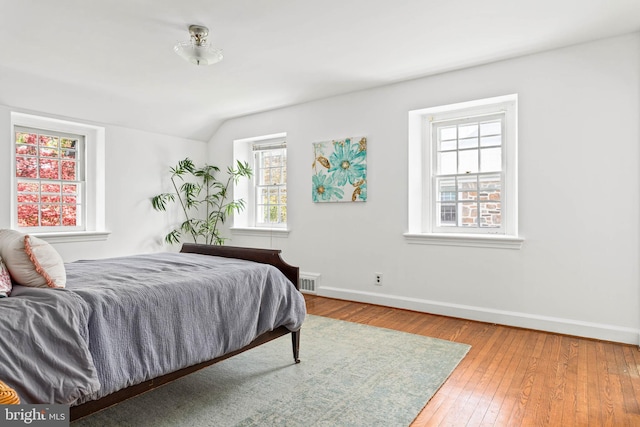 bedroom featuring baseboards, vaulted ceiling, visible vents, and hardwood / wood-style floors