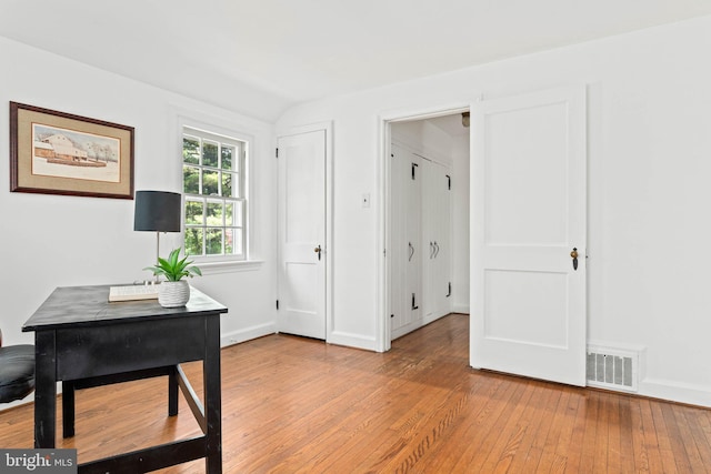 office space featuring baseboards, vaulted ceiling, light wood-type flooring, and visible vents