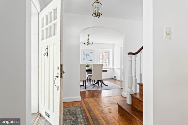 entrance foyer with arched walkways, baseboards, a chandelier, stairs, and hardwood / wood-style floors