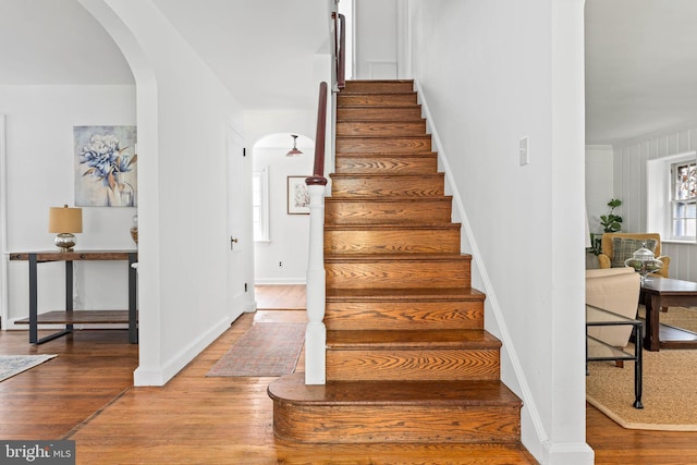 stairway with arched walkways, baseboards, and wood finished floors