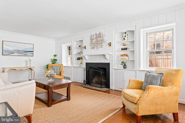 living room with crown molding, built in shelves, hardwood / wood-style floors, a fireplace with flush hearth, and visible vents