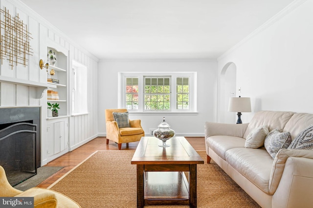 living area with crown molding, built in shelves, baseboards, a fireplace with flush hearth, and wood finished floors