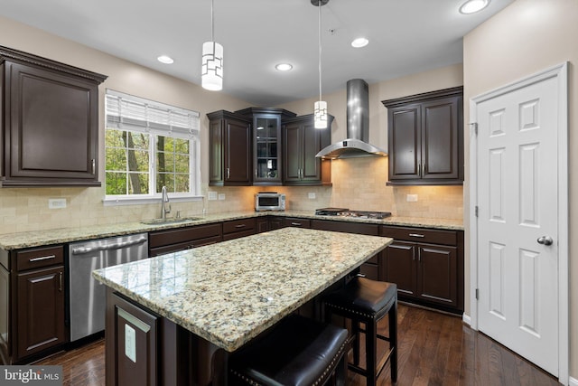 kitchen with a sink, dark brown cabinetry, wall chimney range hood, a breakfast bar, and appliances with stainless steel finishes