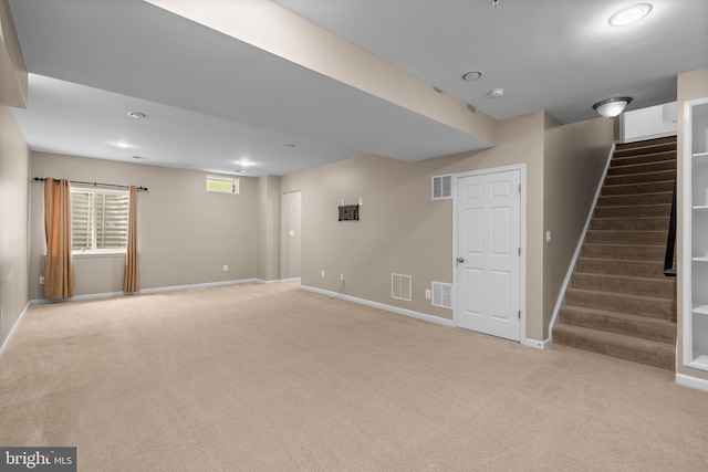 below grade area with baseboards, stairway, visible vents, and light colored carpet