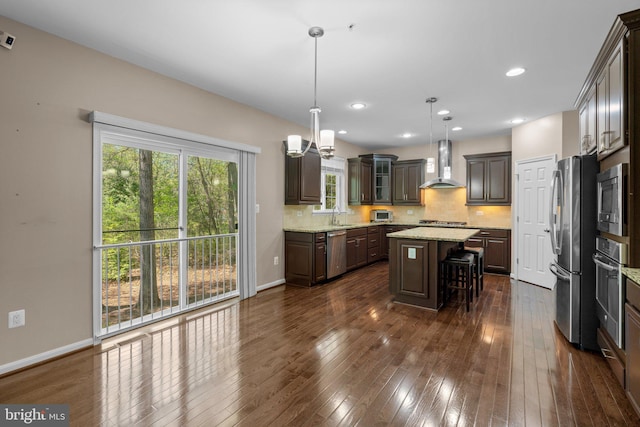 kitchen featuring wall chimney range hood, a center island, dark brown cabinets, a sink, and stainless steel appliances