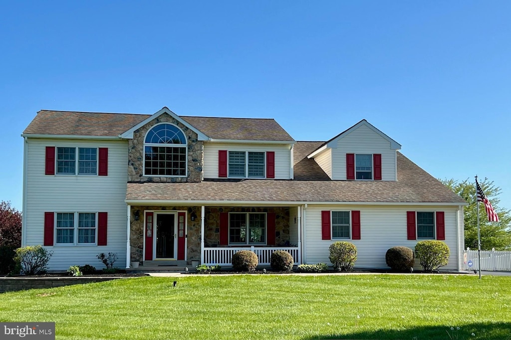 traditional-style house featuring a porch, roof with shingles, stone siding, and a front yard