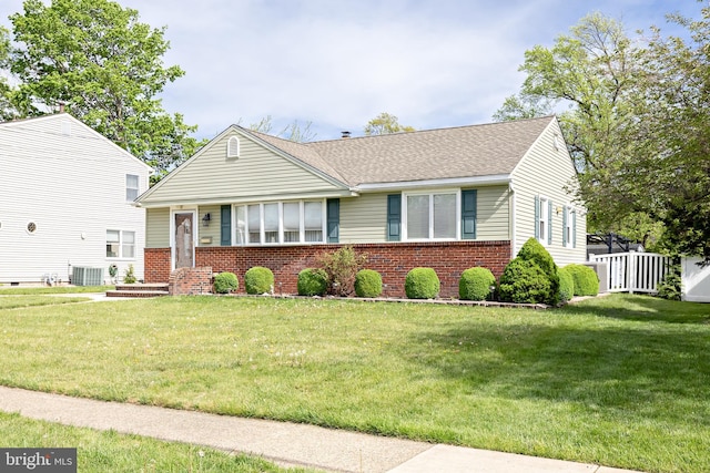 view of front facade featuring a front yard, fence, central air condition unit, and brick siding