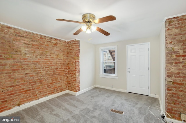 carpeted spare room featuring baseboards, a ceiling fan, brick wall, and visible vents