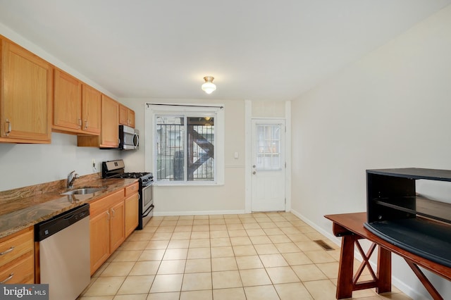 kitchen featuring a sink, baseboards, light tile patterned floors, dark stone countertops, and stainless steel appliances