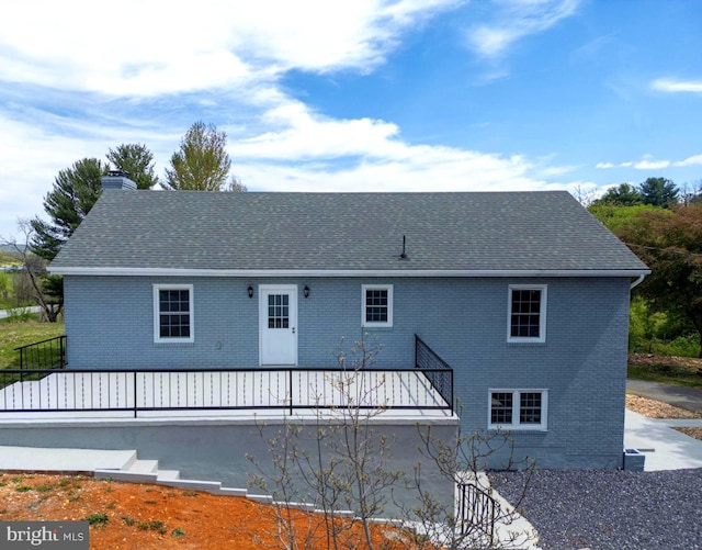 rear view of property with a chimney, brick siding, and roof with shingles