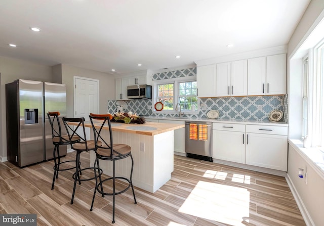 kitchen with a center island, white cabinetry, backsplash, light countertops, and appliances with stainless steel finishes