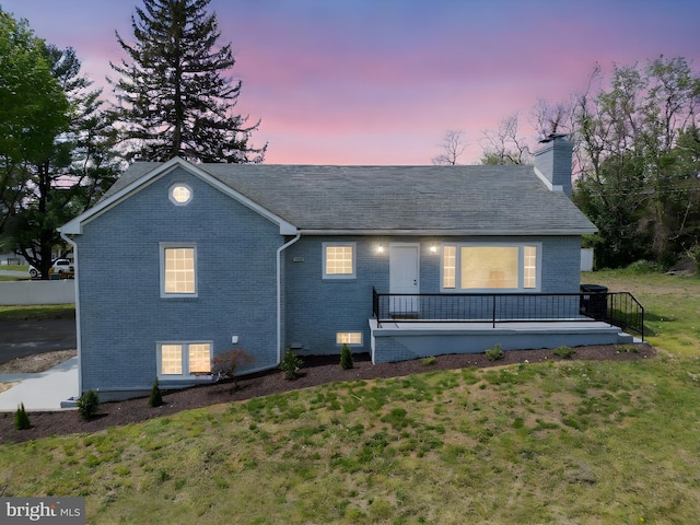 view of front of property with a wooden deck, a chimney, brick siding, and a front yard