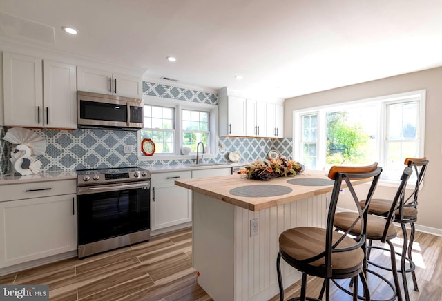 kitchen featuring light wood-style flooring, a sink, appliances with stainless steel finishes, wooden counters, and a breakfast bar area
