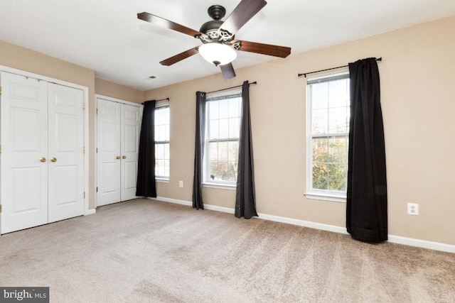unfurnished bedroom featuring two closets, carpet flooring, and baseboards