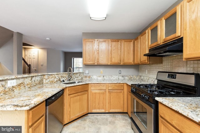kitchen featuring light stone counters, under cabinet range hood, stainless steel appliances, a sink, and decorative backsplash