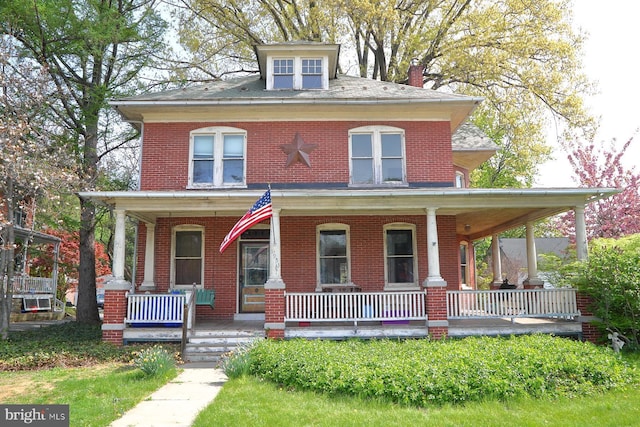 view of front of home with covered porch, a chimney, and brick siding