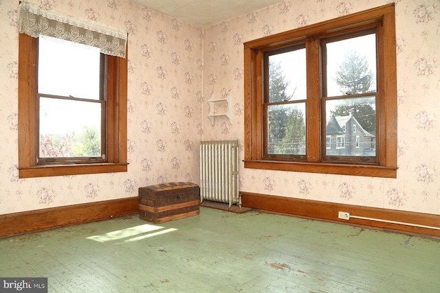 unfurnished room featuring baseboards, radiator heating unit, hardwood / wood-style flooring, and a healthy amount of sunlight