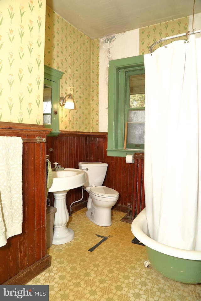 full bathroom featuring a wainscoted wall, wallpapered walls, a tub, toilet, and tile patterned floors