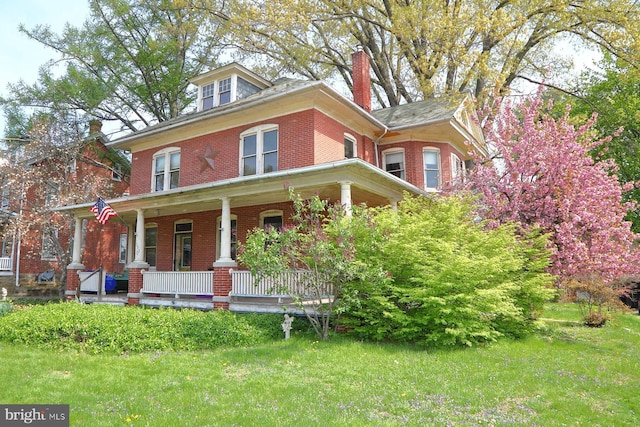 view of front of property featuring a chimney, brick siding, a porch, and a front lawn