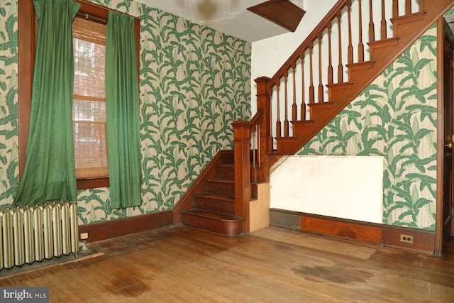 staircase featuring radiator, wallpapered walls, wood finished floors, and baseboards