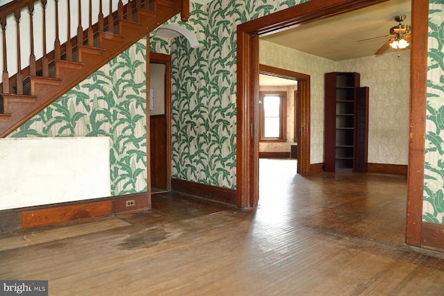 staircase with wood finished floors, ceiling fan, wallpapered walls, and baseboards