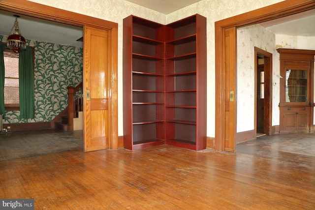 spare room featuring stairs, wallpapered walls, wood finished floors, and baseboards