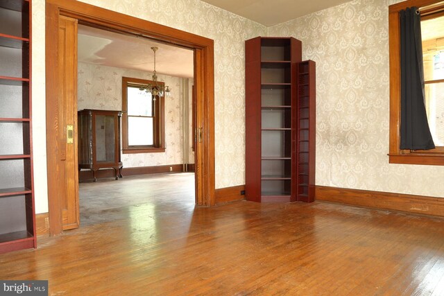 unfurnished room with an inviting chandelier, wallpapered walls, and wood finished floors