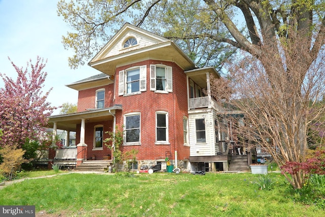victorian home with covered porch, a front yard, brick siding, and a balcony