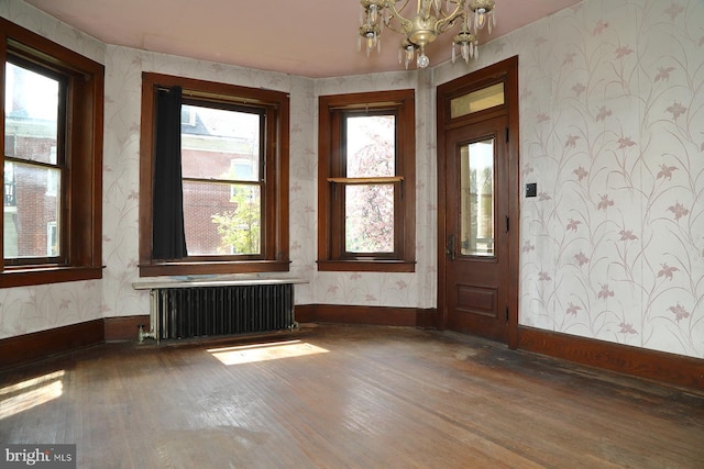 foyer entrance with wood finished floors, wallpapered walls, radiator heating unit, baseboards, and a notable chandelier