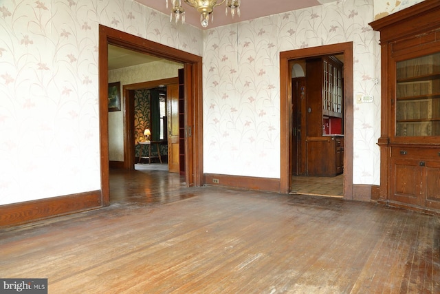 unfurnished room featuring an inviting chandelier, hardwood / wood-style flooring, wallpapered walls, and baseboards