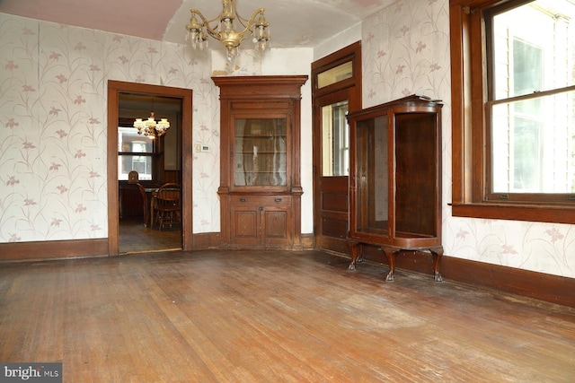 unfurnished room with baseboards, wallpapered walls, wood finished floors, and an inviting chandelier