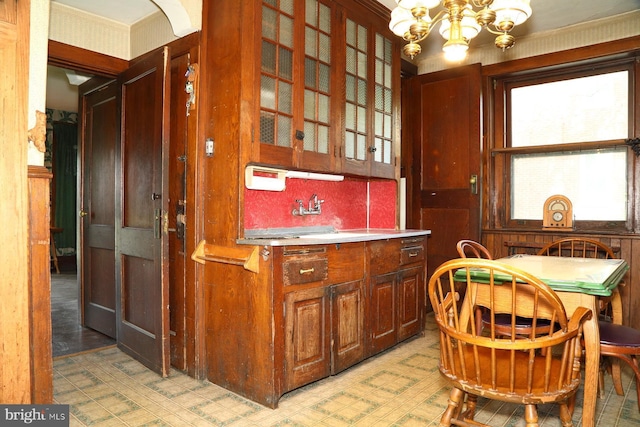 kitchen with a sink, glass insert cabinets, a notable chandelier, light countertops, and light floors