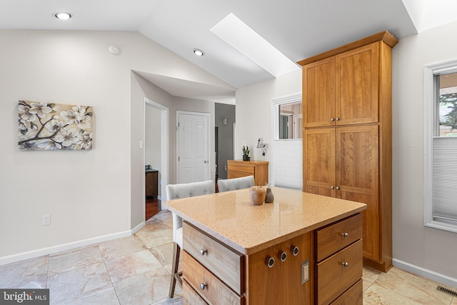 kitchen with lofted ceiling, light stone countertops, a kitchen island, and baseboards