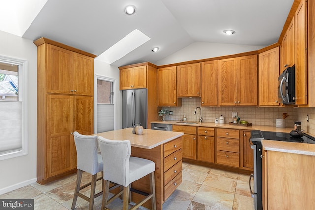 kitchen featuring decorative backsplash, a sink, a breakfast bar, stainless steel appliances, and lofted ceiling with skylight