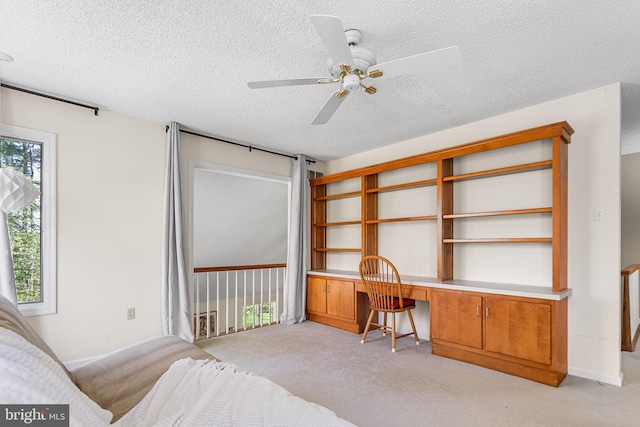 bedroom with a textured ceiling, ceiling fan, light colored carpet, and built in desk