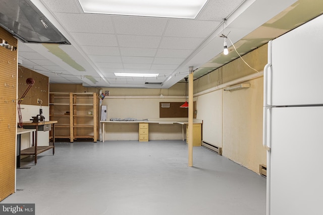 below grade area featuring a paneled ceiling, baseboard heating, and freestanding refrigerator