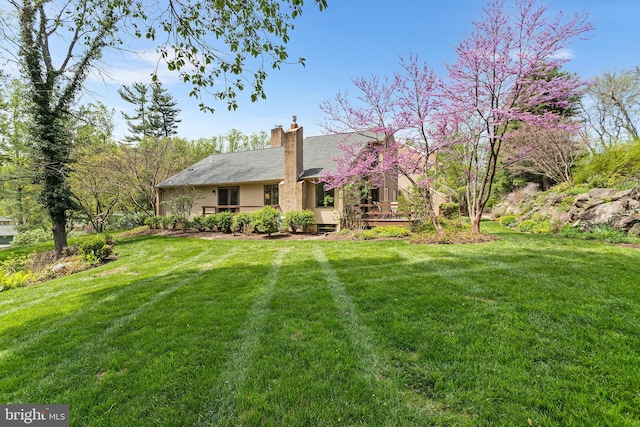 ranch-style home with a chimney, a wooden deck, and a front lawn
