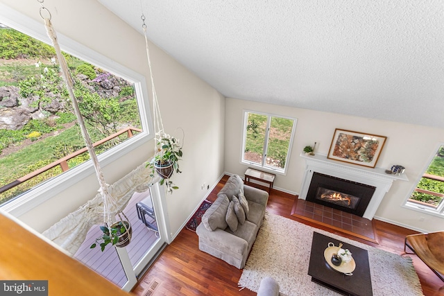 living room featuring a textured ceiling, visible vents, baseboards, a fireplace, and wood finished floors