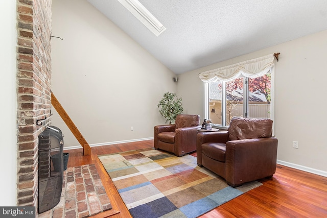 living area featuring wood finished floors, baseboards, a wood stove, and vaulted ceiling with skylight