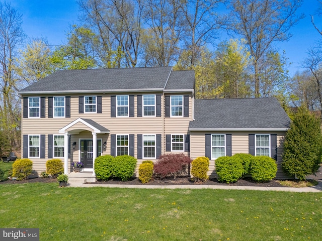 colonial home with a shingled roof and a front yard