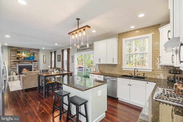 kitchen with a sink, dark wood finished floors, dark stone counters, stainless steel appliances, and open floor plan