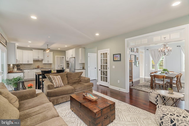 living area with recessed lighting, baseboards, an inviting chandelier, and dark wood-type flooring