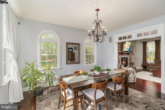 dining area featuring a notable chandelier, wood-type flooring, a glass covered fireplace, a healthy amount of sunlight, and visible vents