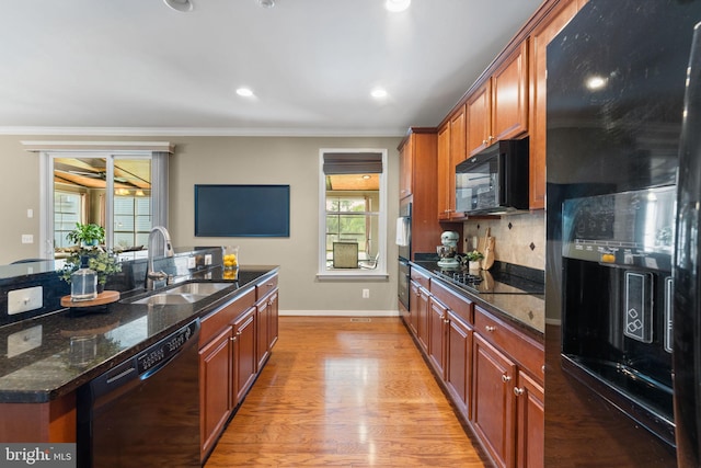 kitchen featuring dark stone counters, a sink, light wood-style flooring, backsplash, and black appliances