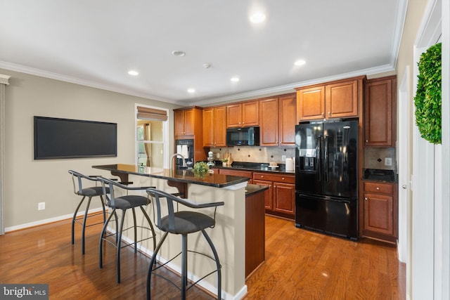 kitchen with decorative backsplash, black appliances, a kitchen bar, and wood finished floors