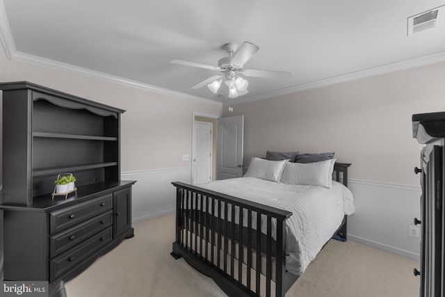 bedroom featuring ceiling fan, visible vents, crown molding, light colored carpet, and wainscoting