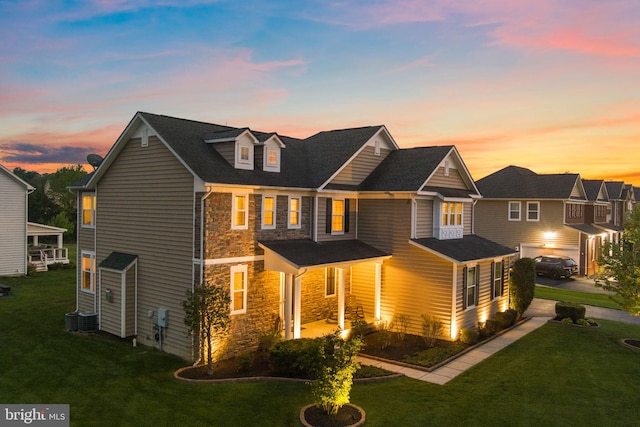 rear view of property featuring a lawn, stone siding, and a garage